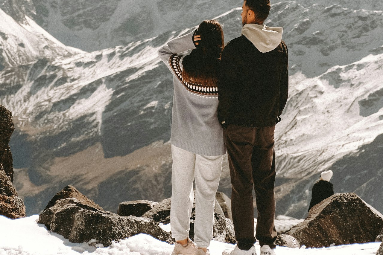 Two travellers looking out across a snow-covered mountain range